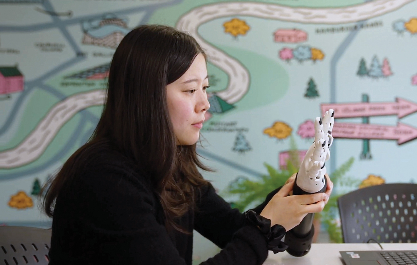 A researcher in a lab, looking and holding a robotic hand. A researcher in a lab, looking and holding a robotic hand.